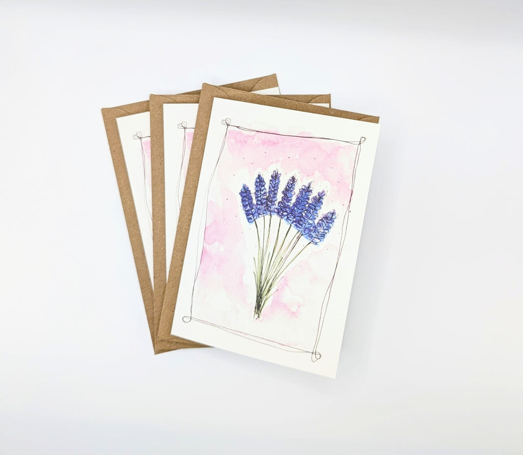 Hand-painted watercolour greeting card featuring a bunch of lavender stems on a blush pink background with an ink border, shown with kraft envelopes