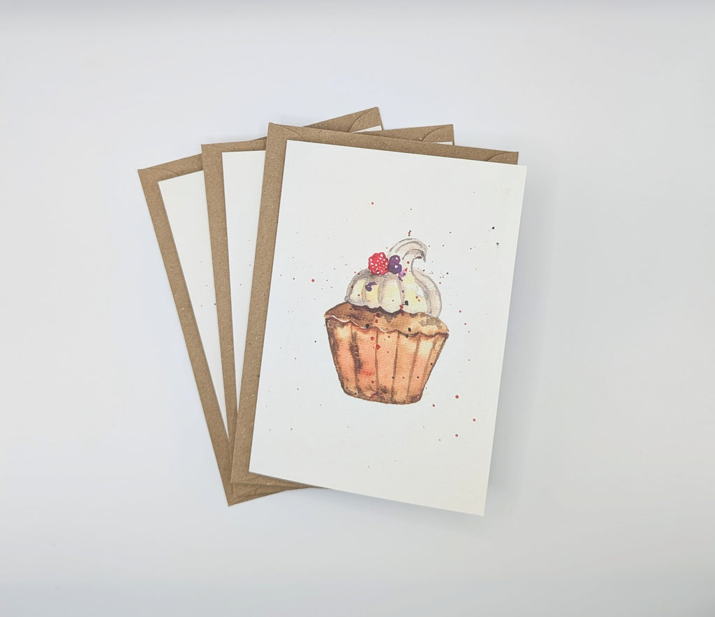 Hand-painted watercolour greeting card featuring a detailed cupcake with cream swirl and berry topping, shown with kraft envelopes