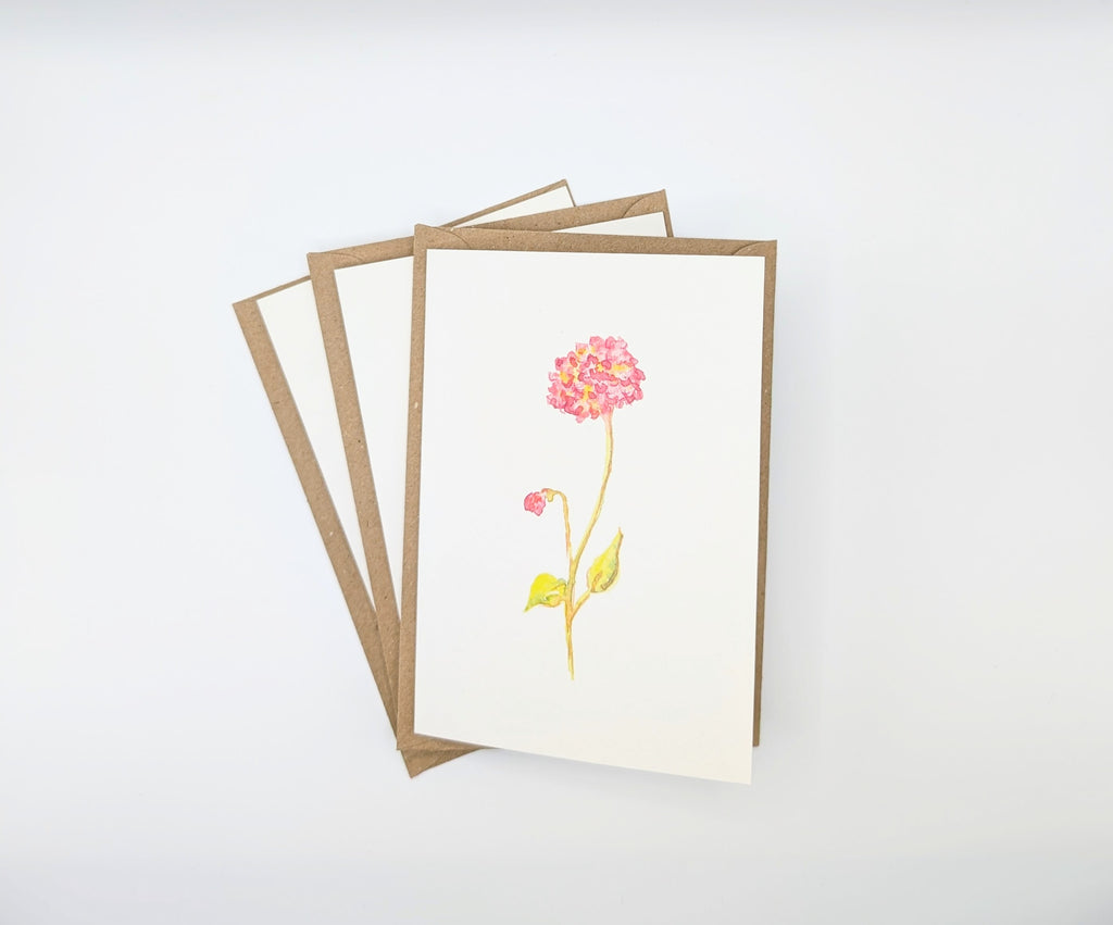 Hand-painted watercolour greeting card featuring a single pink bloom on a slender stem with a small bud, shown with kraft envelopes