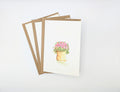 Hand-painted watercolour greeting card featuring a terracotta pot overflowing with tiny pink flowers and green foliage, shown with kraft envelopes