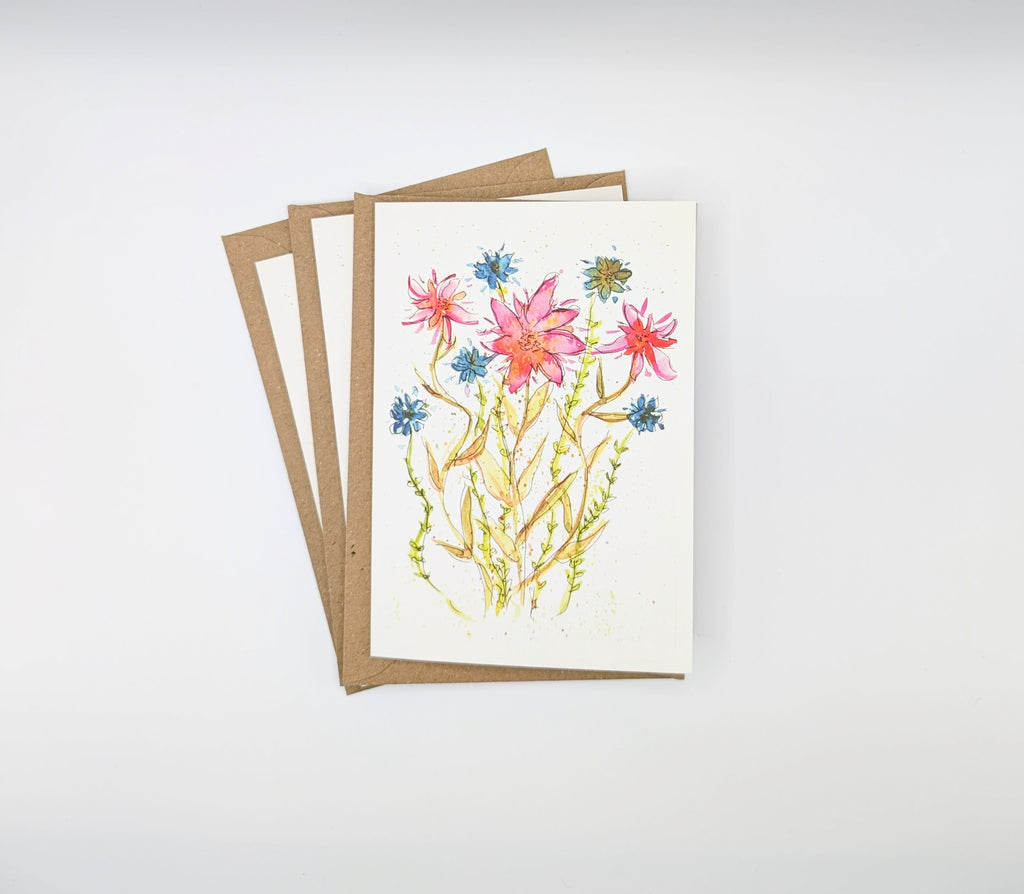 Hand-painted watercolour greeting card featuring wild pink and blue flowers with expressive ink stems, shown with kraft envelopes